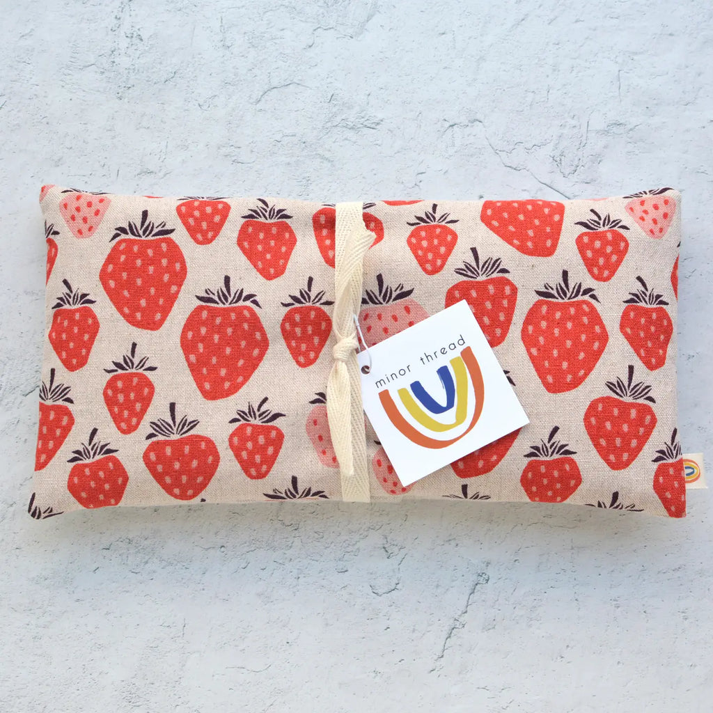 Fabric pouch with strawberry print and branding label on a textured background.