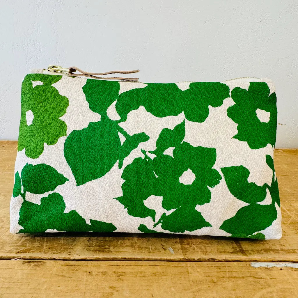 A green and white floral patterned clutch purse on a wooden surface.