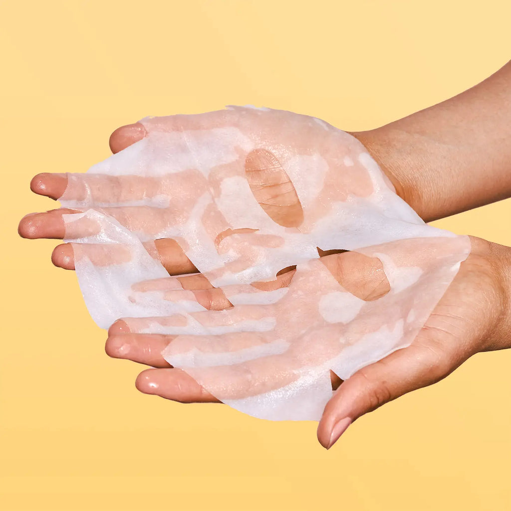 Hands holding a translucent, peeling facial mask against a yellow background.