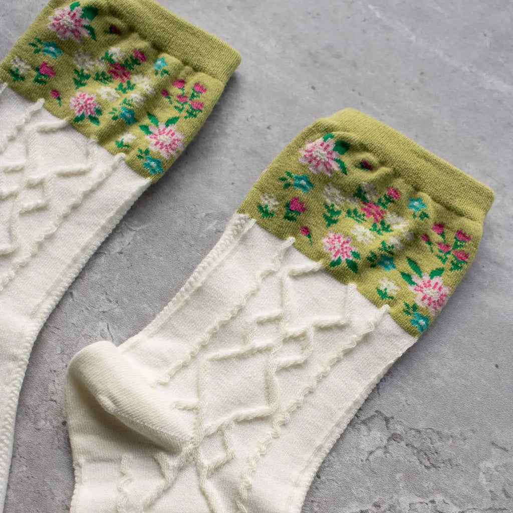 A pair of white socks with a green toe and floral design on a grey background.