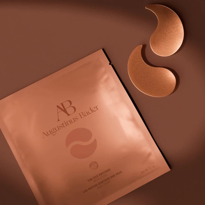 A pack of augustinus bader skincare products with eye mask patches on a brown surface.