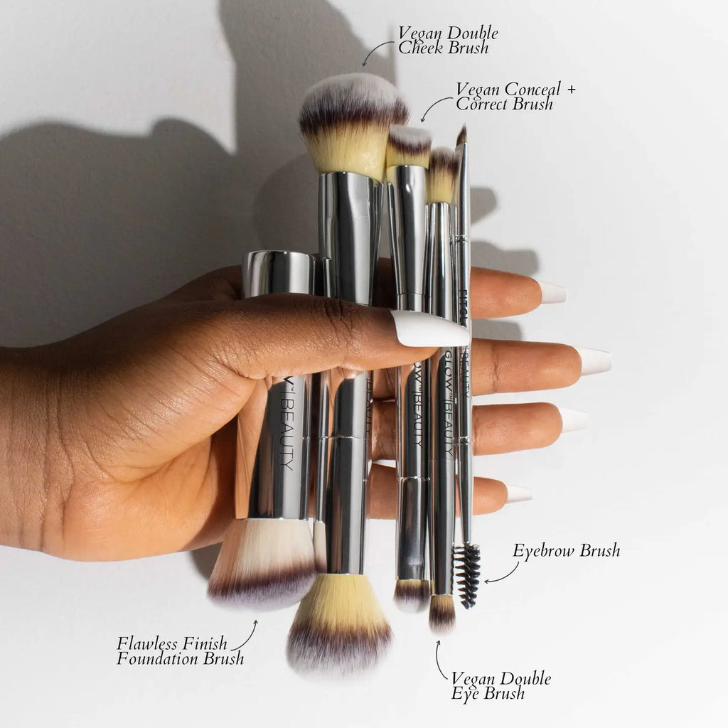 A hand holding the Fitglow Beauty Master Brush Set, which includes a Flawless Finish Foundation Brush, Vegan Double Cheek Brush, Vegan Conceal + Correct Brush, Eyebrow Brush, and Vegan Double Eye Brush. This versatile vegan brush set pairs perfectly with an Eco Makeup Bag for all your beauty needs.