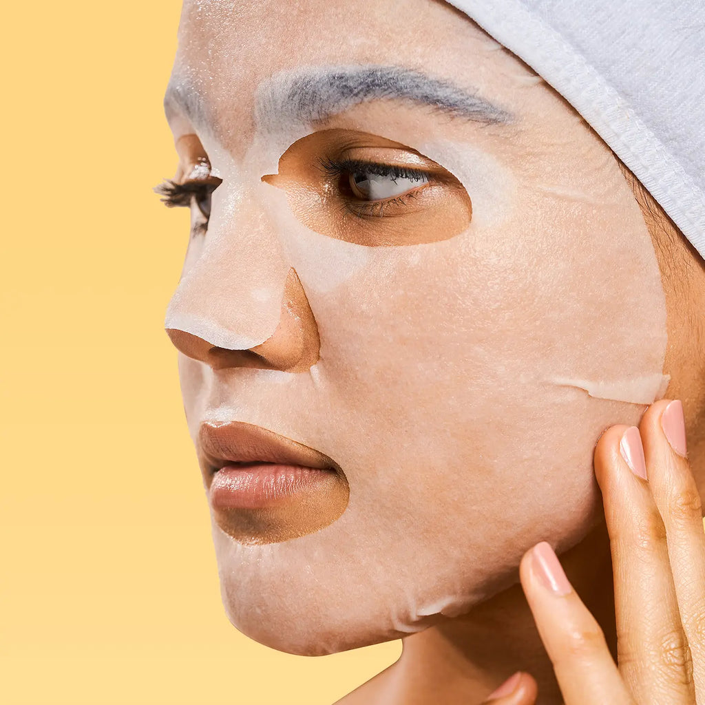 Woman with a facial mask sheet applied to her face against a yellow background.