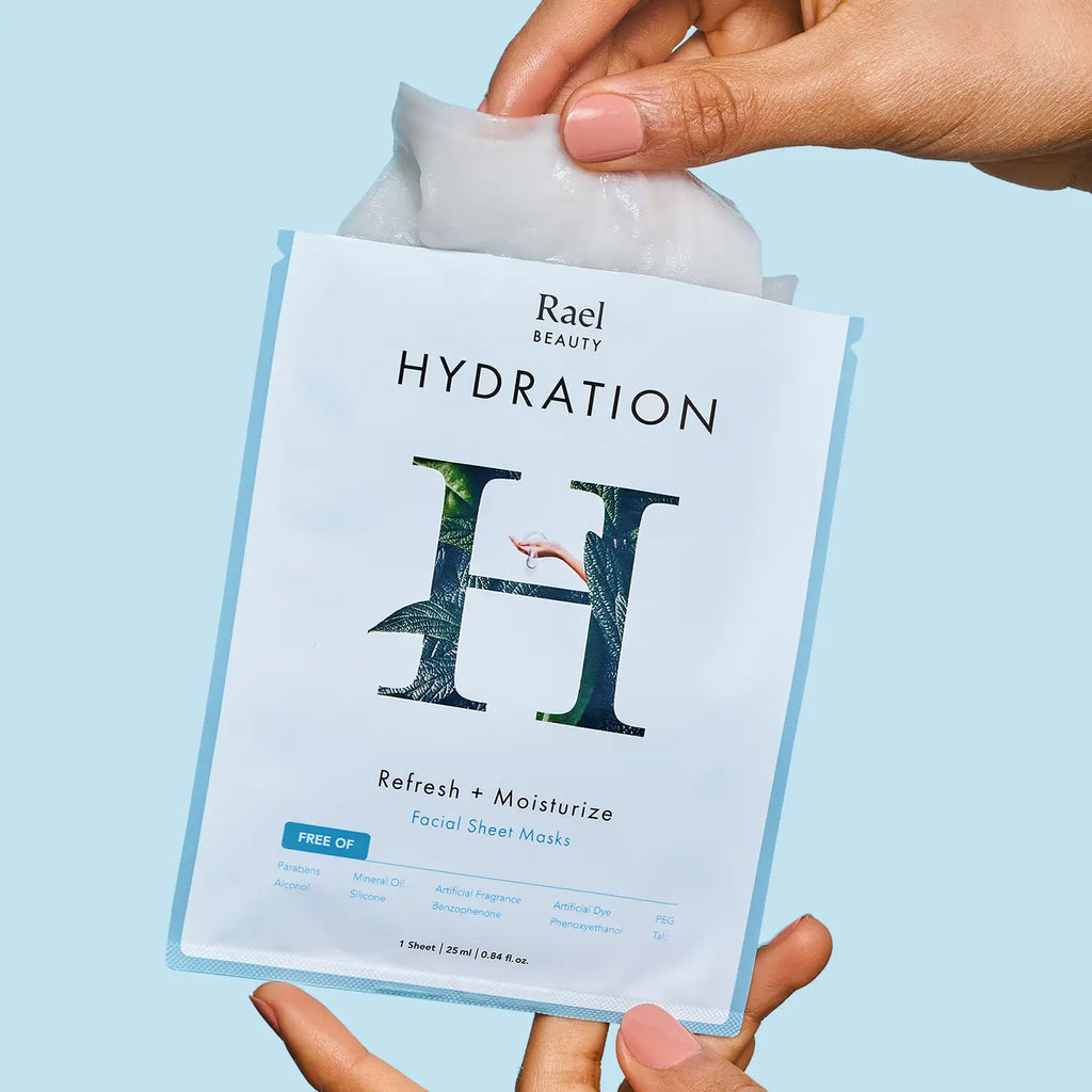 Hands holding a rael beauty hydration facial sheet mask packet against a blue background.