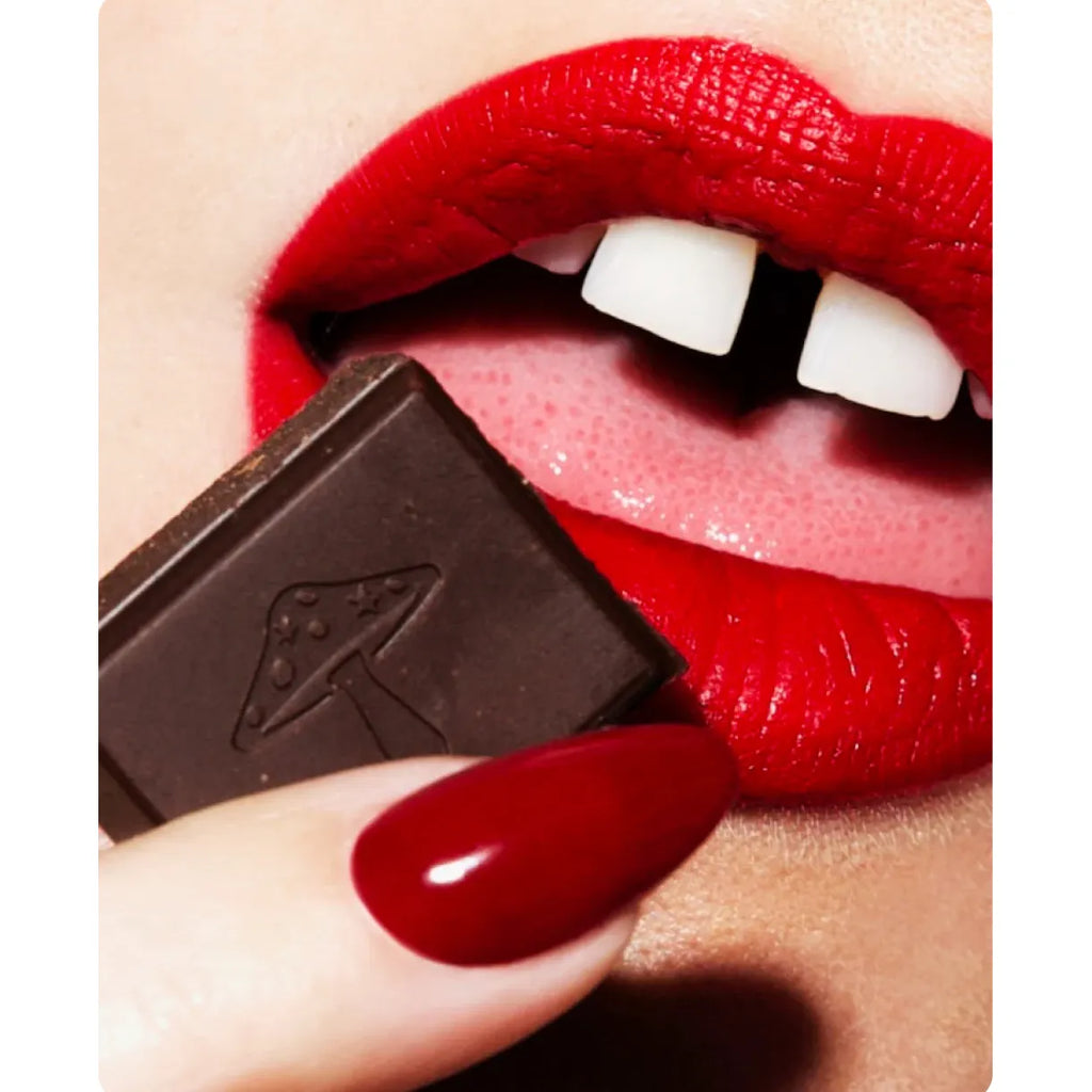 Close-up of red-lipped mouth biting a piece of dark chocolate.