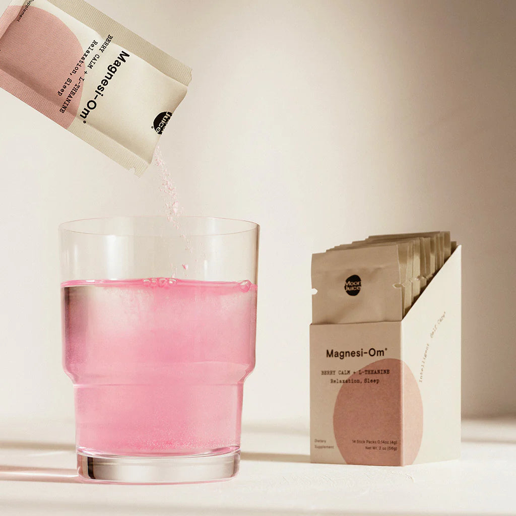 A packet of pink powder being poured into a glass of water next to its product packaging.