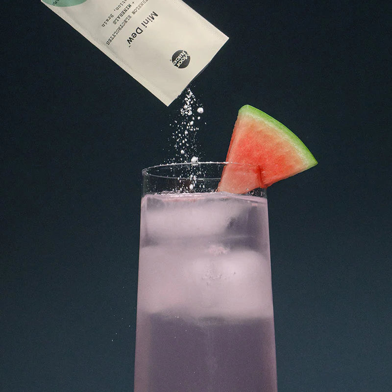 Sugar being poured into a glass of purple liquid with a watermelon slice on the rim.