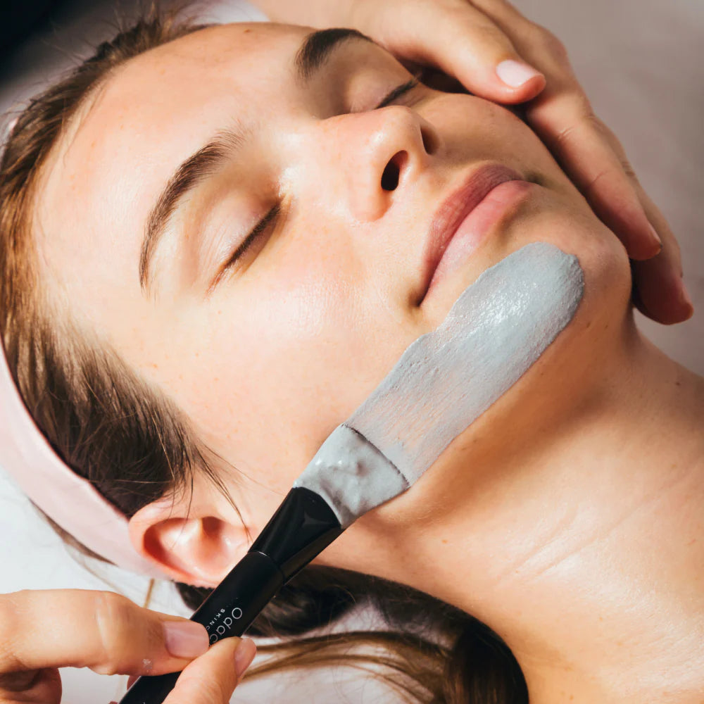 Application of a facial mask with a brush on a woman's face during a skincare treatment.