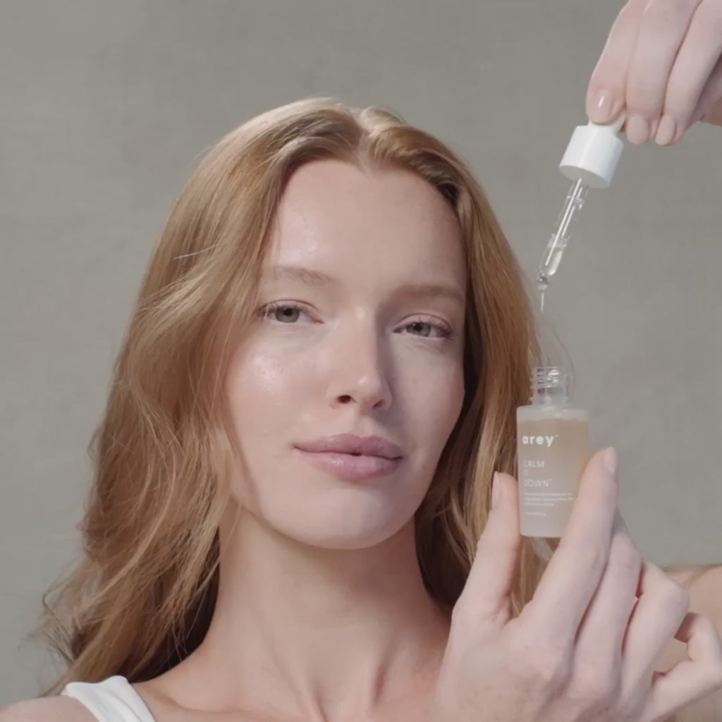 Woman with strawberry blonde hair applying Arey's Calm It Down Scalp Serum
