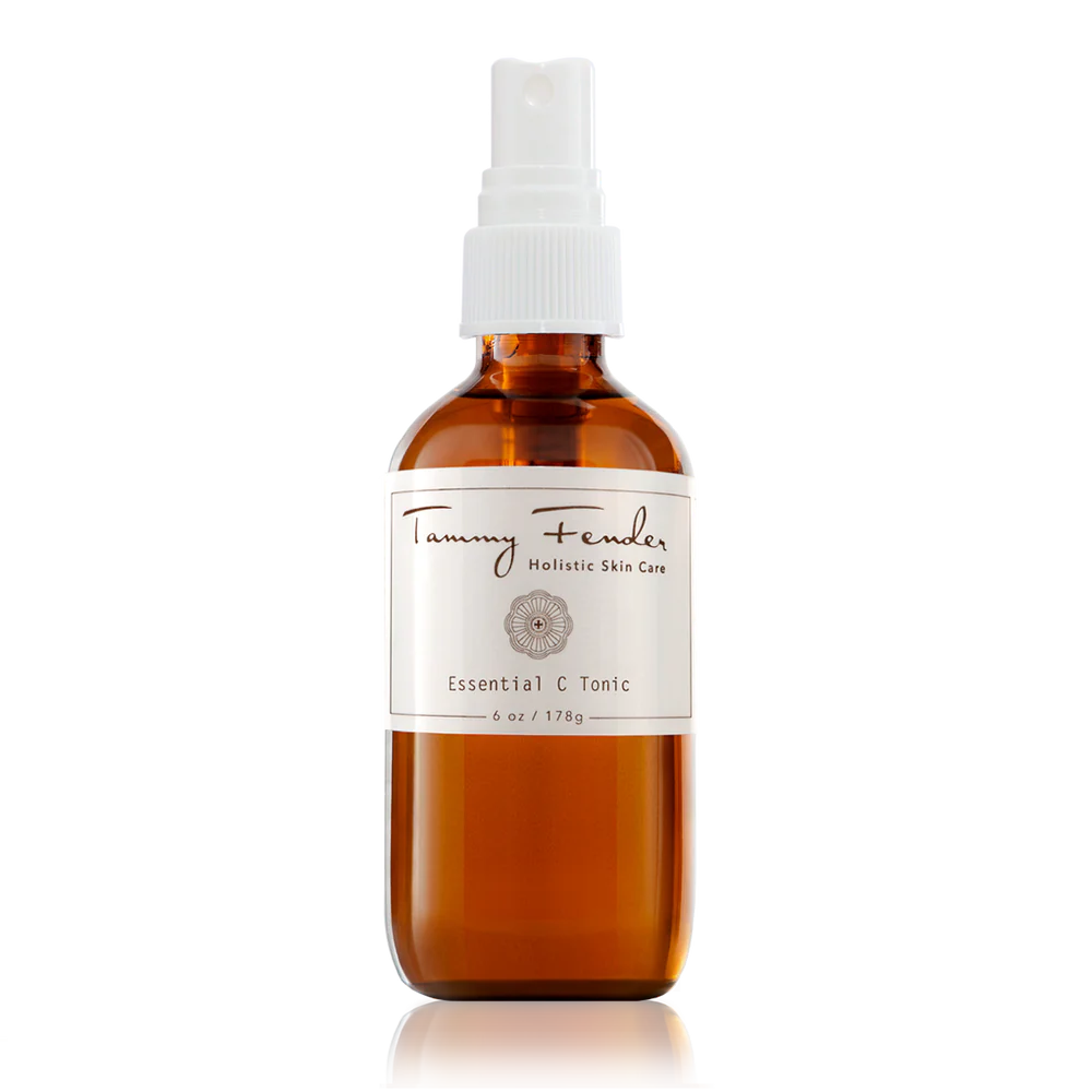 Amber glass bottle with spray nozzle labeled "tammy fender holistic skin care essential tonic" against a black and white background.