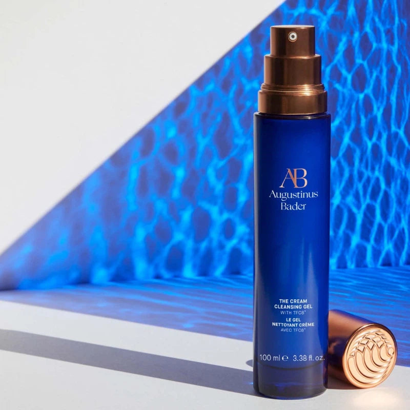 A bottle of augustinus bader face cream against a patterned blue background.