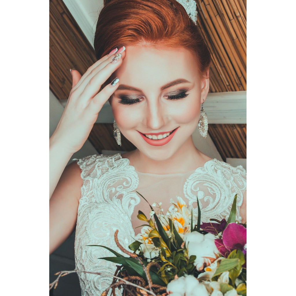 A smiling bride holding a bouquet with her left hand on her forehead.