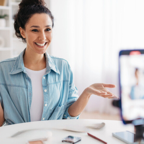 A smiling woman in a denim shirt gesturing during a video call.