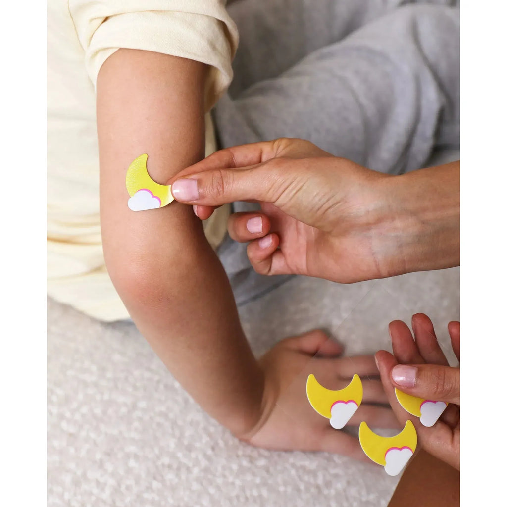Applying a moon and cloud-shaped adhesive bandage to a child's elbow.