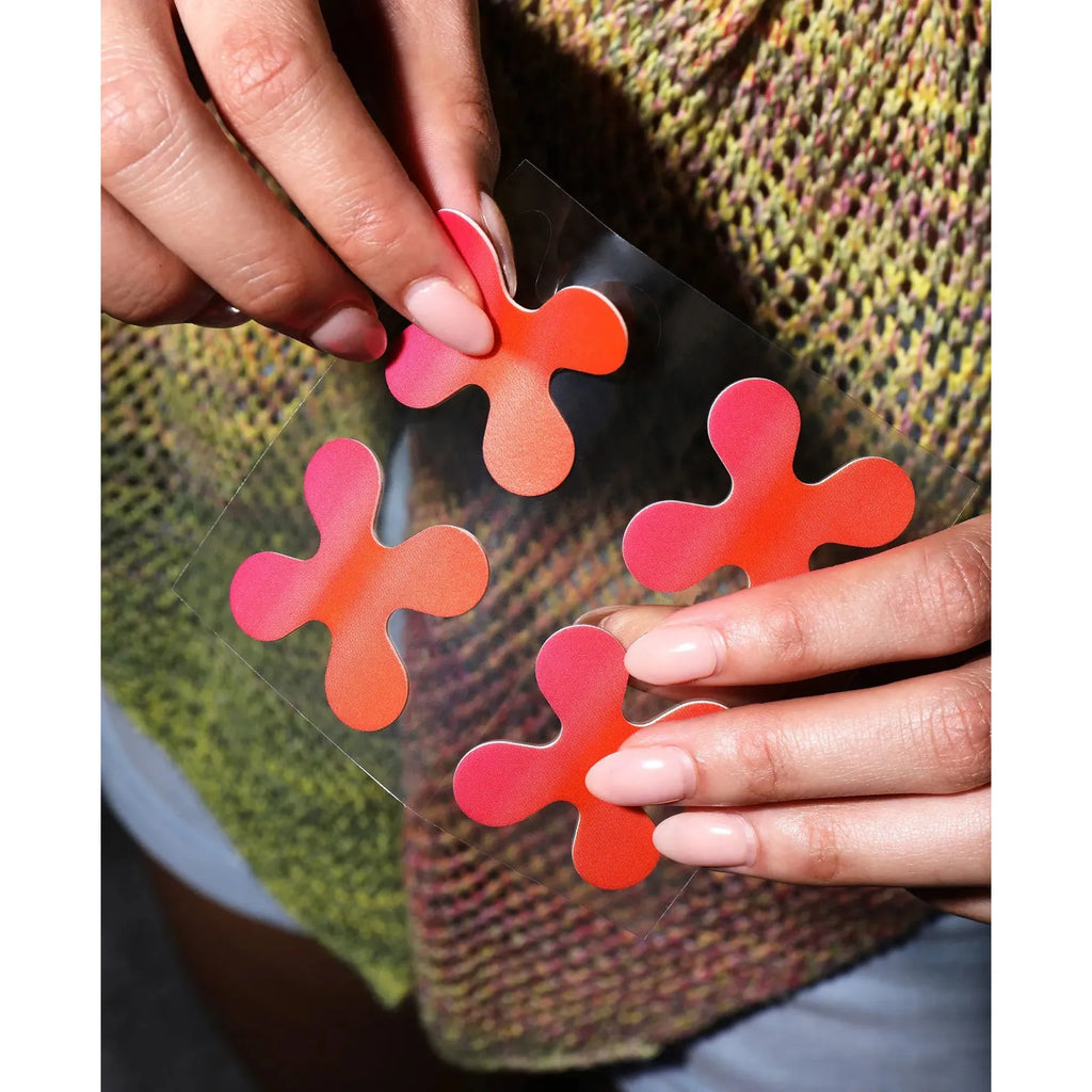 Hands holding transparent sheet with three colorful adhesive notes in shape of splats against a multicolored textile background.