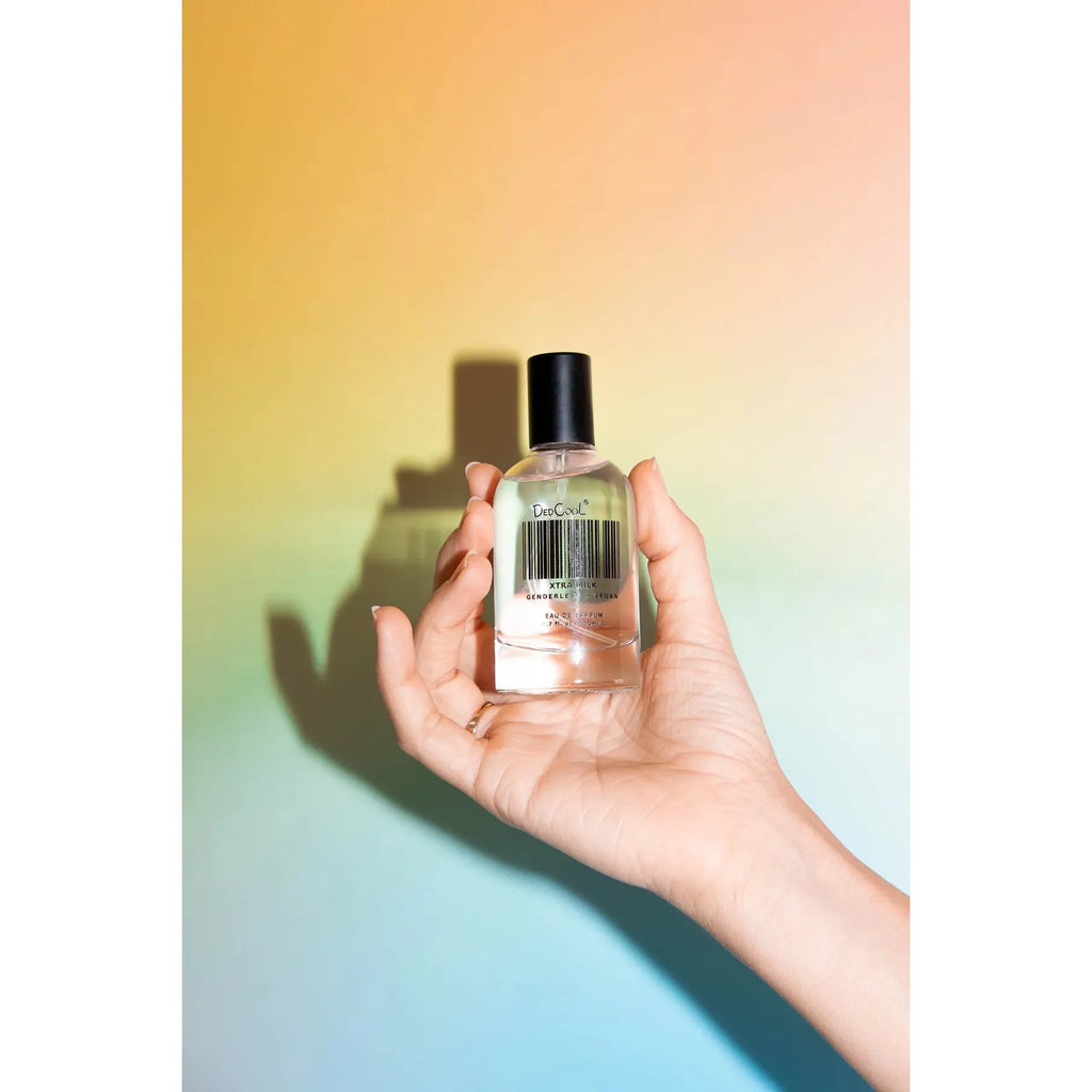A hand holding a clear bottle of nail polish against a colorful gradient background.