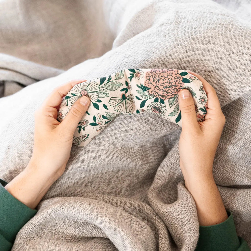 A person holding a floral-patterned sleep mask over a cozy blanket.