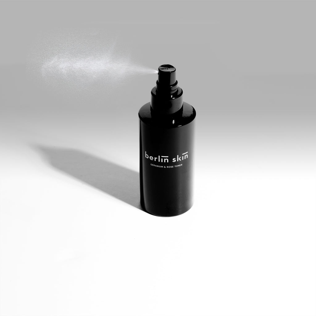 Black spray bottle with mist being dispensed against a white background.