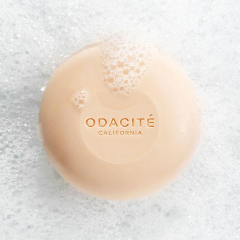 A bar of odacite soap resting on a textured surface with bubbles.