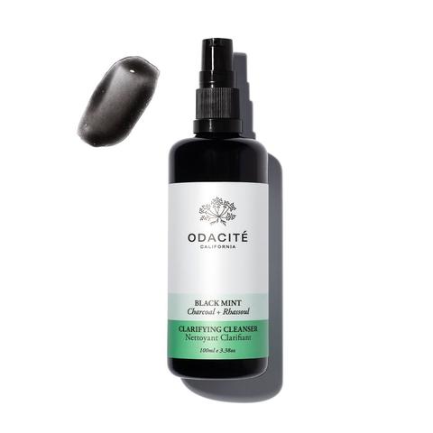 Bottle of odacite black mint cleanser with a mint leaf and charcoal piece.