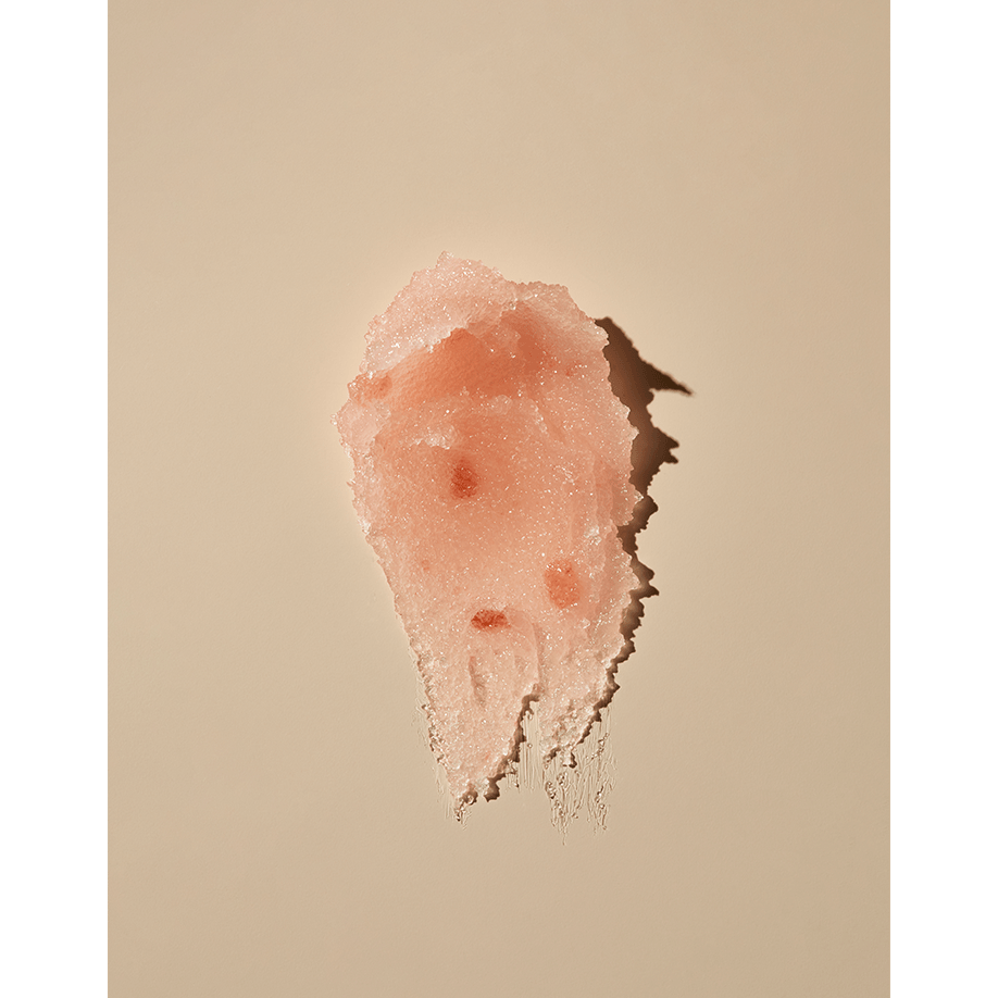 A smear of pink facial scrub on a beige background.