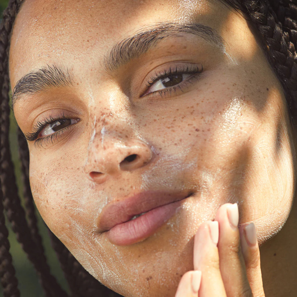 Close-up of a woman with freckles, touching her face gently.