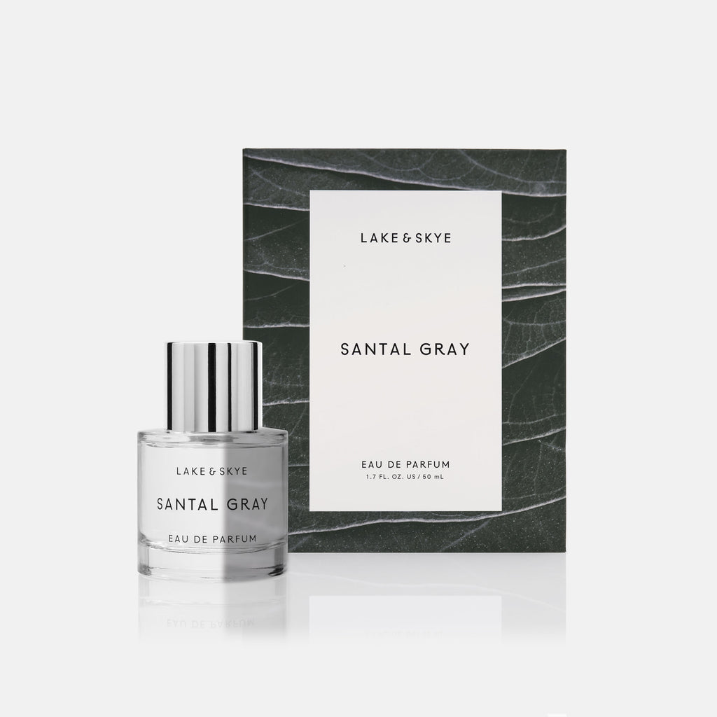 A bottle of "santal gray" eau de parfum by lake & skye in front of its packaging with a marble background.