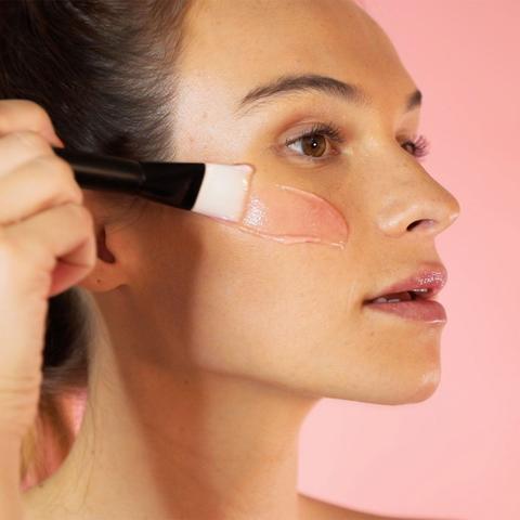 Applying liquid foundation to cheek with makeup brush.