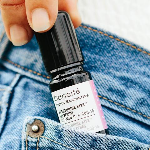 Close-up of a hand holding a bottle of odacite lip serum against a denim background.