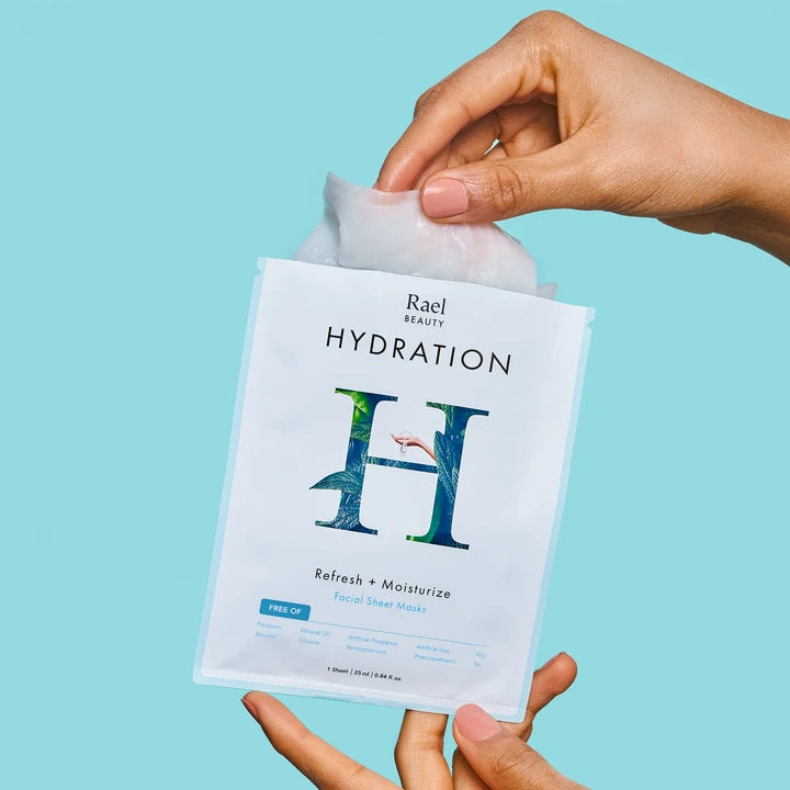 A person's hands pulling a facial sheet mask out of its rael beauty hydration packaging against a turquoise background.