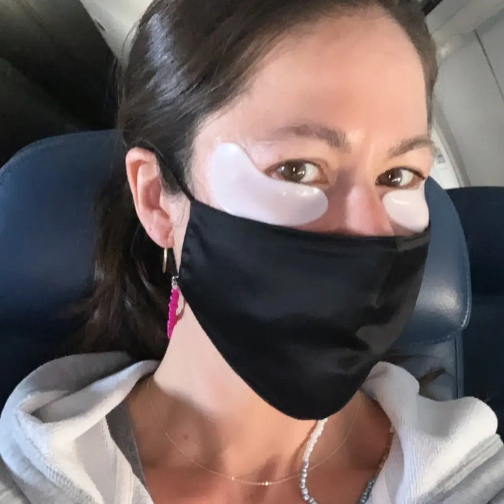 Woman wearing a face mask and under-eye patches while seated in an airplane cabin.