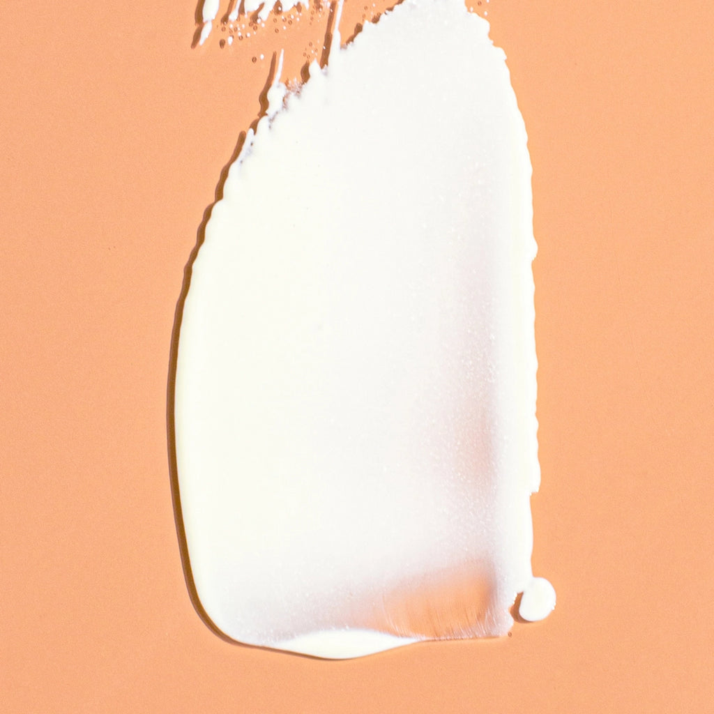 A swatch of liquid foundation makeup smeared on a peach-colored background.