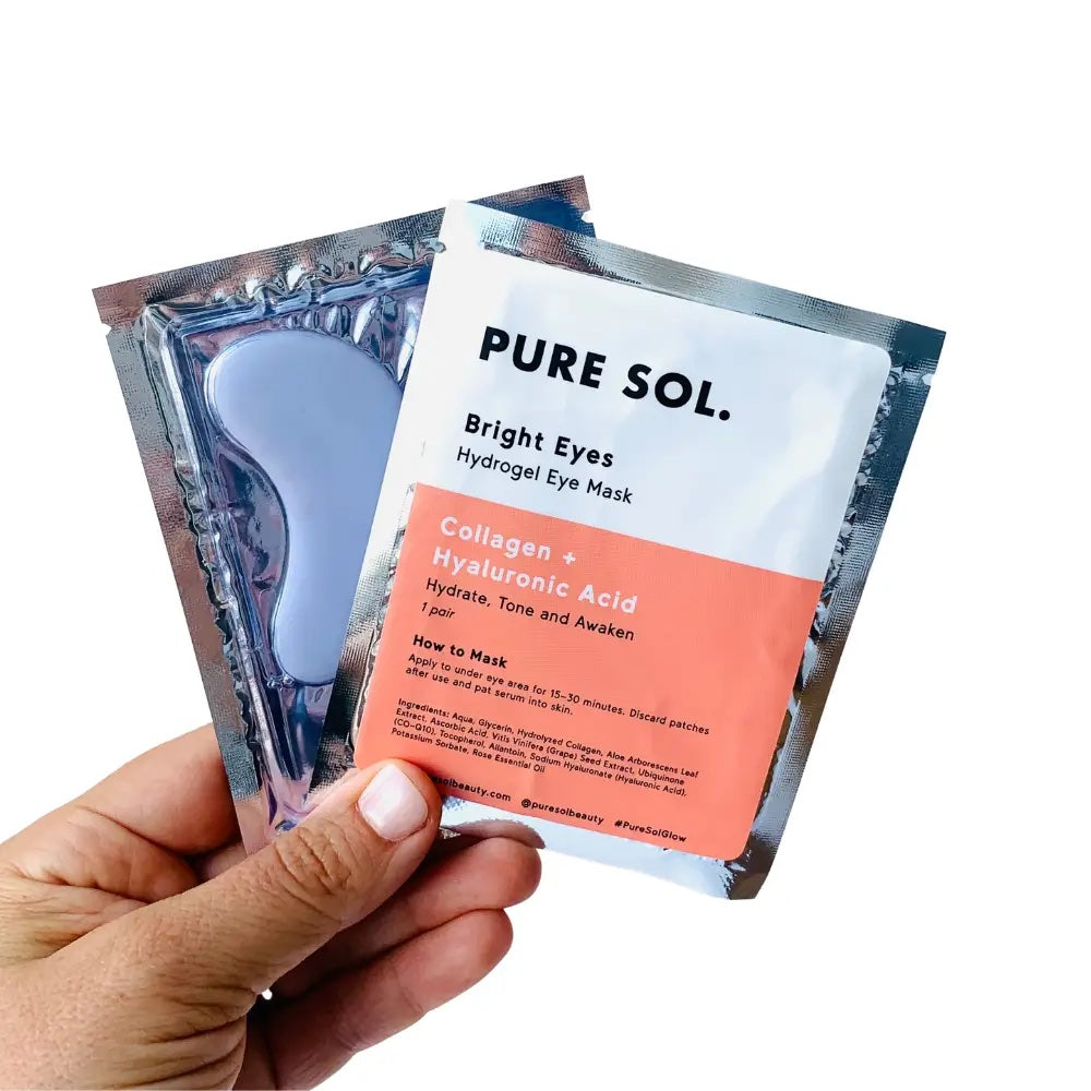 A hand holding two packets of pure sol. bright eyes mask with collagen and hyaluronic acid.