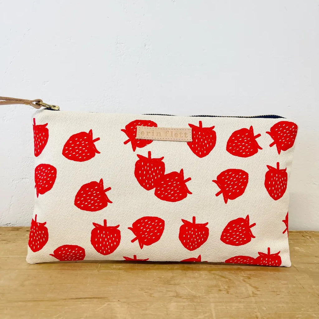 White cosmetic pouch with red strawberry print design on a beige surface.