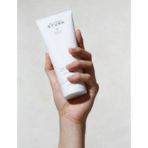 A hand holding a tube of cosmetic cream against a neutral background.