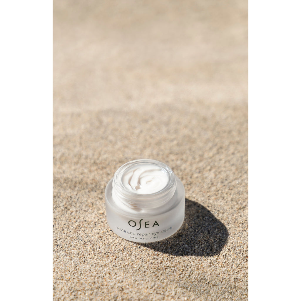 A jar of osea advanced repair eye cream on a sandy background.