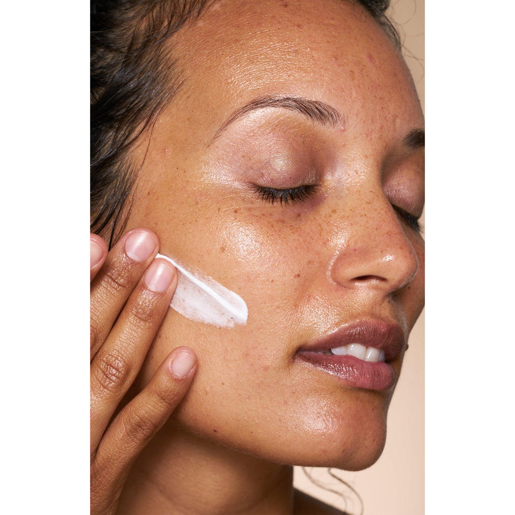 Applying facial moisturizer to clear skin.