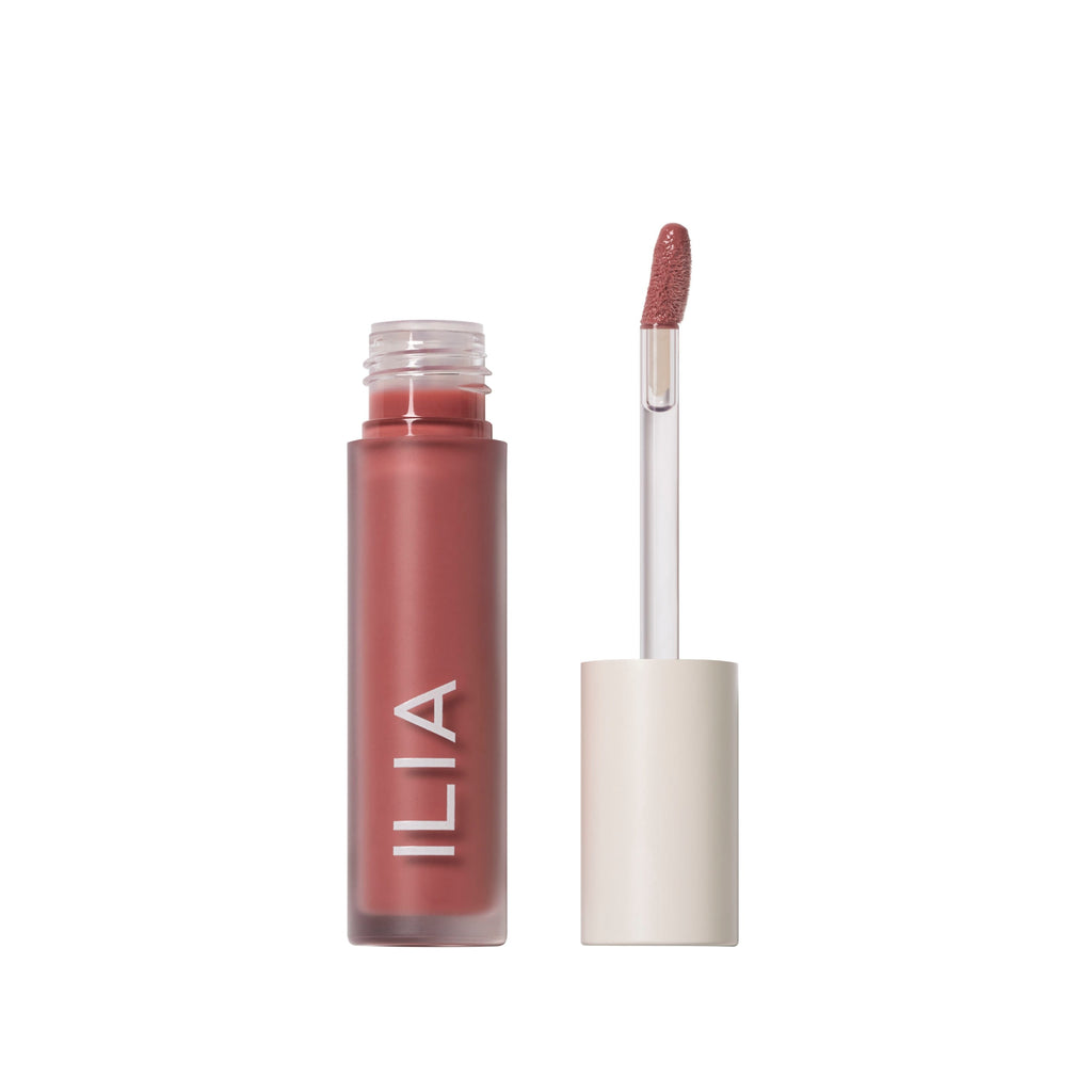A tube of ilia brand lip gloss with an applicator wand next to it.