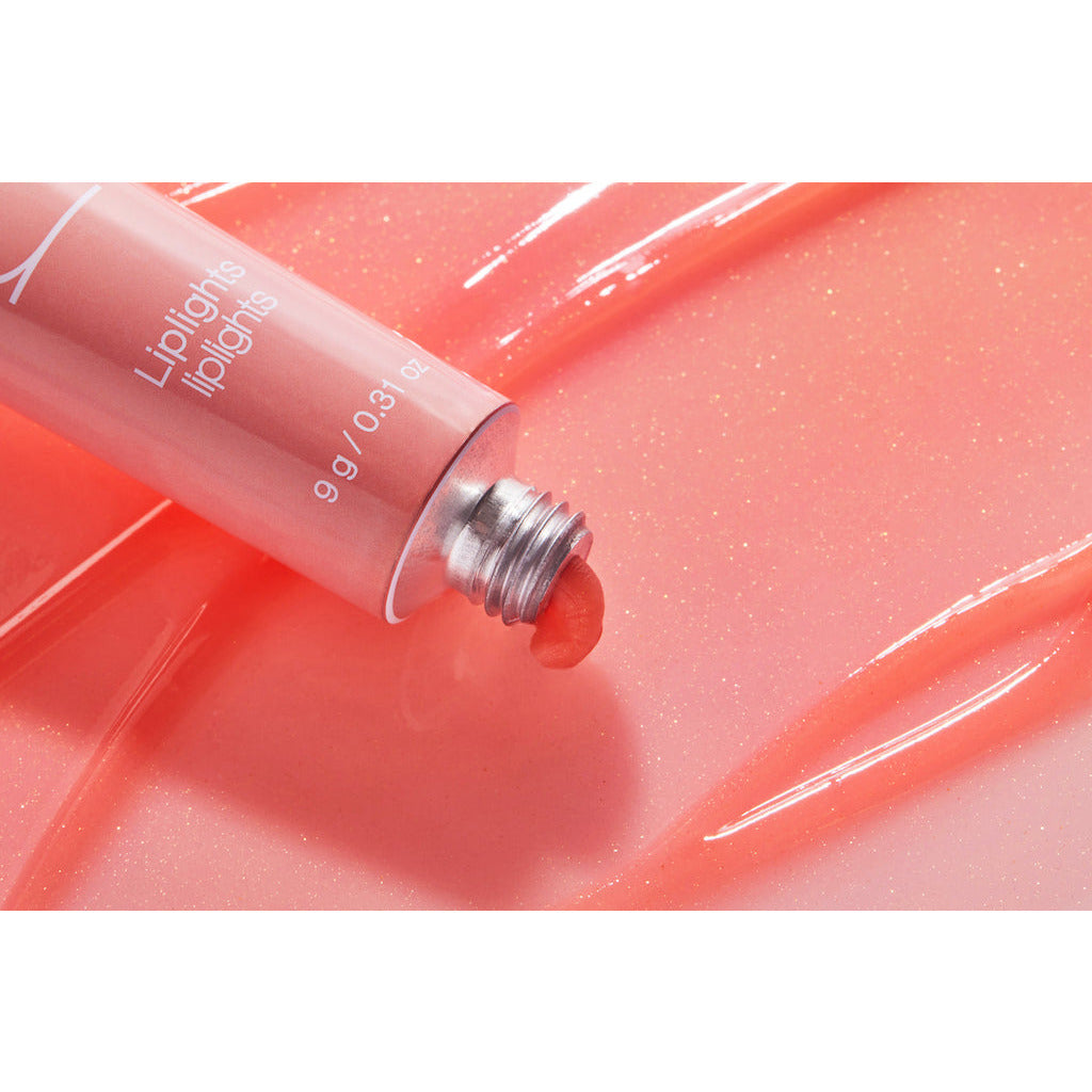 A tube of pink lip gloss opened with product smeared on a shiny surface.
