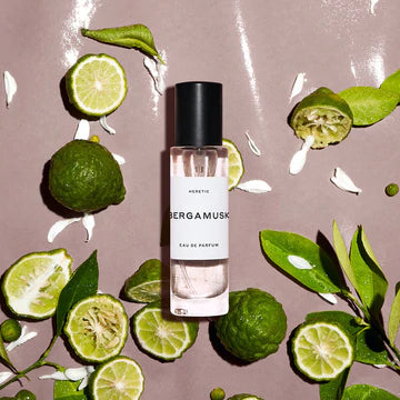 Bottle of bergamusk perfume surrounded by fresh lime slices and leaves on a pink surface.