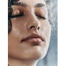Close-up of a person's face with eyes closed and water droplets on the skin.