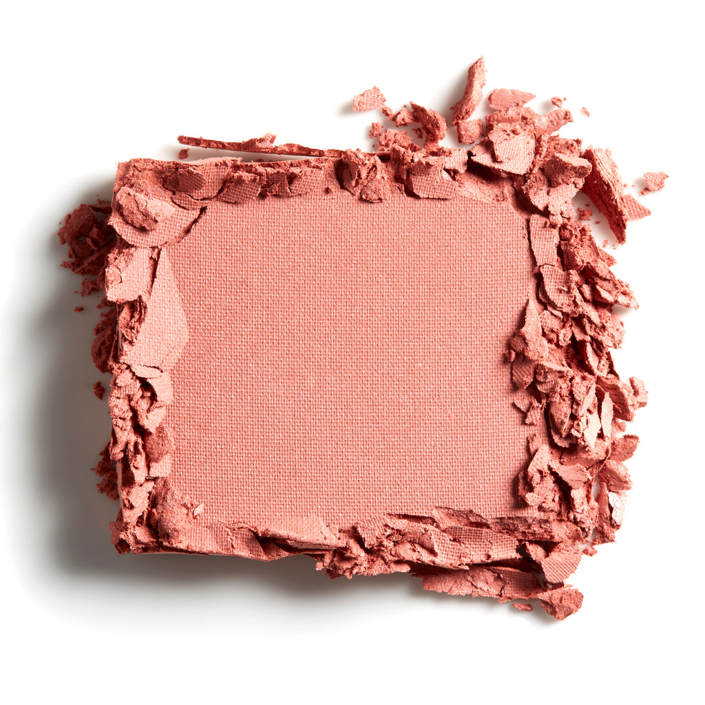 A close-up of a crushed powder blush compact with scattered pieces around the edges.