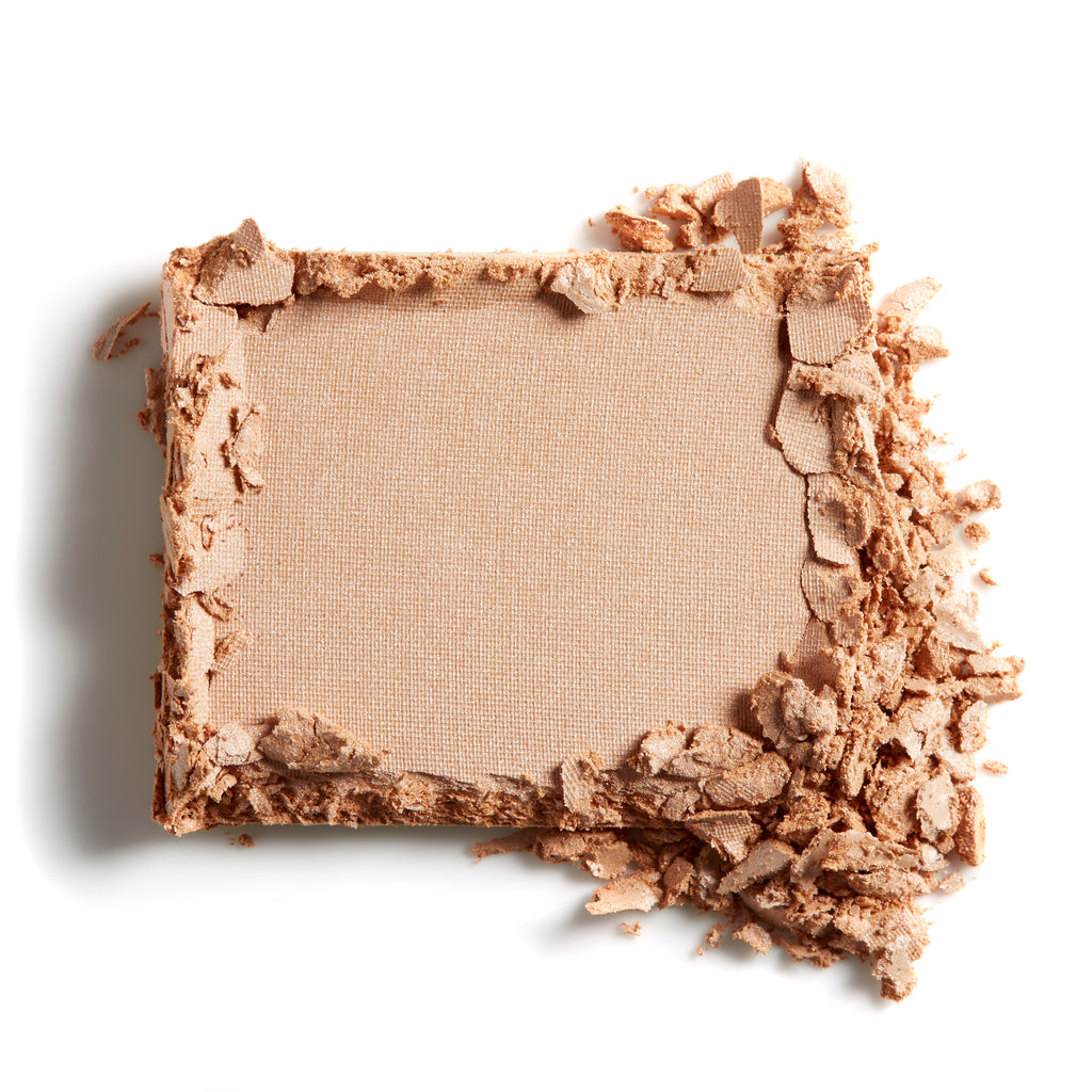 A square of beige powder makeup with some of the product crumbled at the edge.