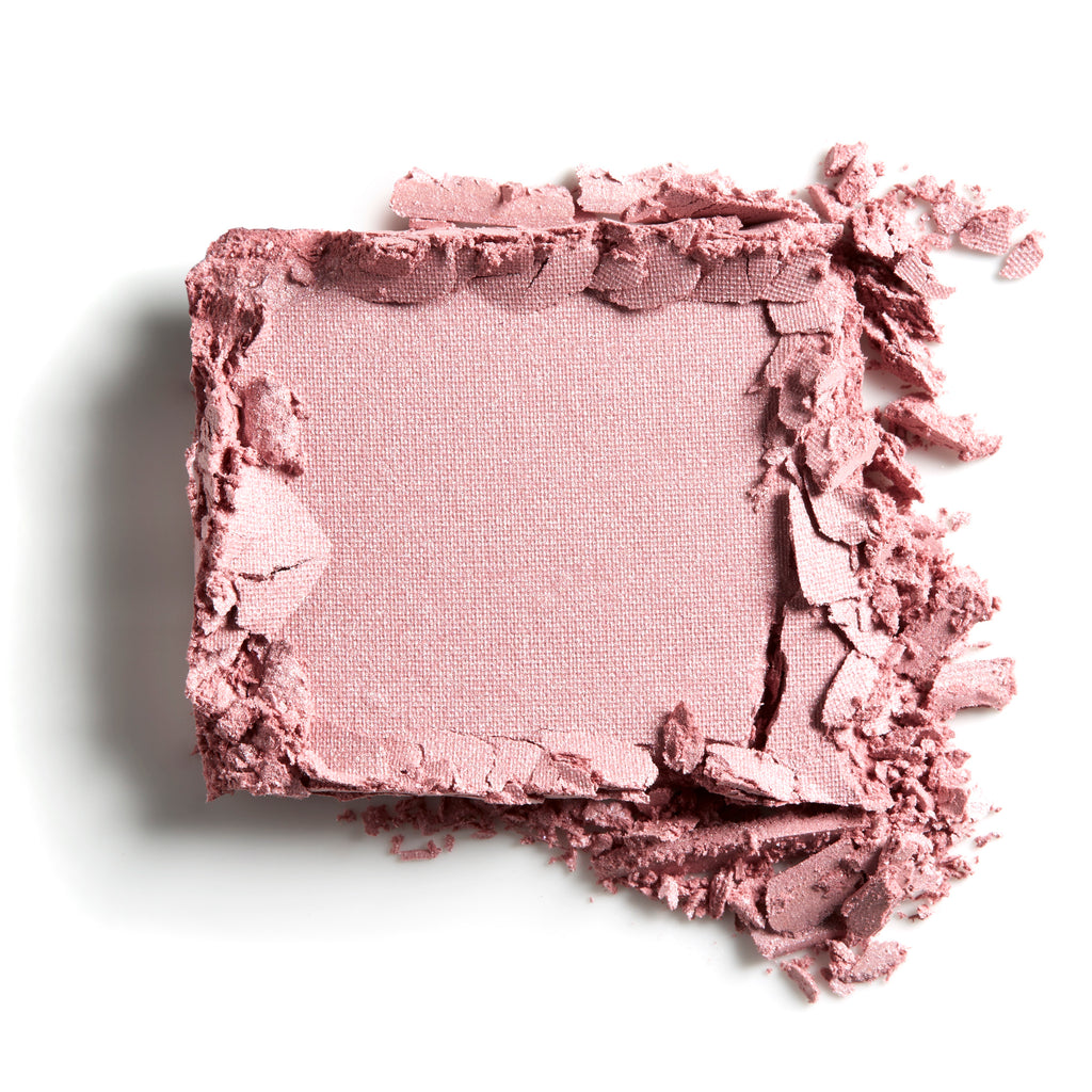 A close-up of a crushed powder blush makeup with pieces scattered around.