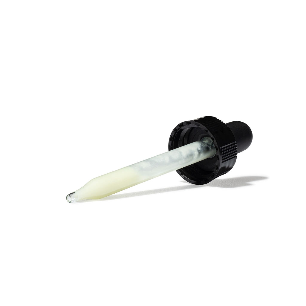Glass dropper with translucent liquid lying on a white surface.