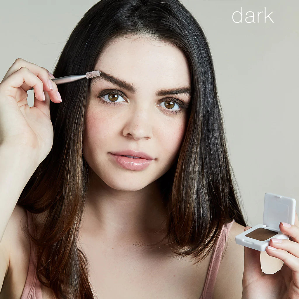 Woman applying eyebrow makeup while holding a compact mirror.