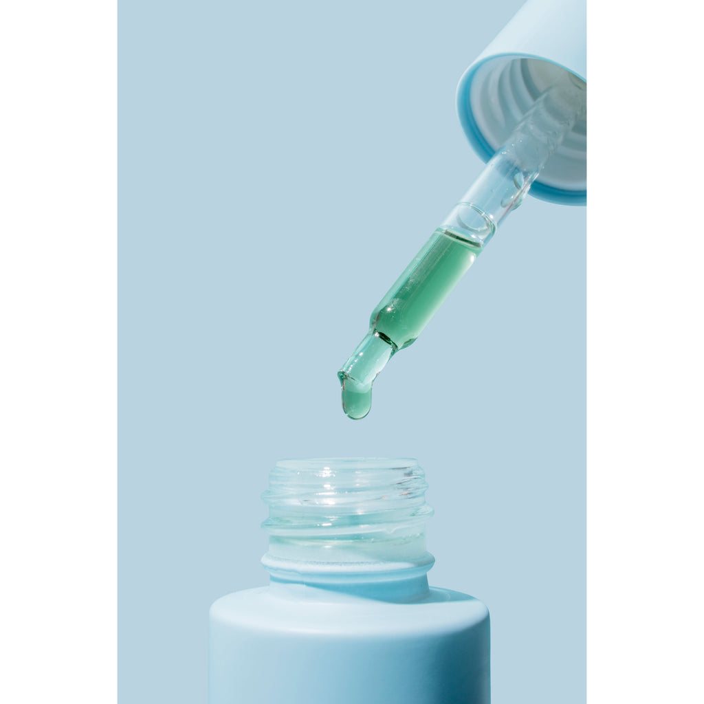 A dropper dispensing liquid into a small container against a blue background.