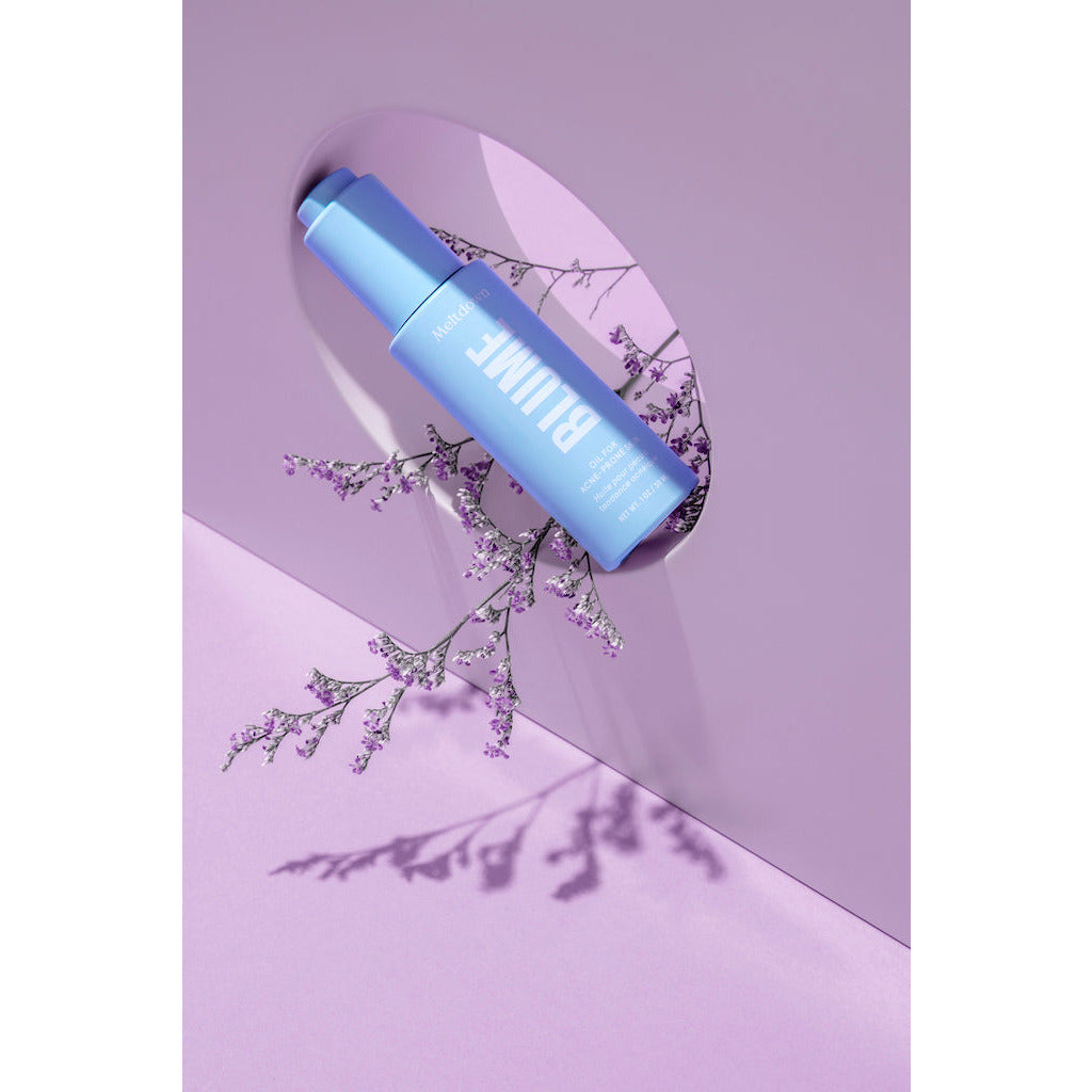 A blue cosmetic bottle with an elegant purple floral arrangement casting a shadow on a pastel background.