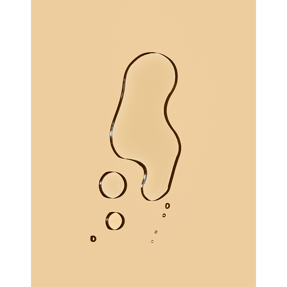 A drop of liquid, possibly oil, in a shape reminiscent of a footprint, on a beige surface.