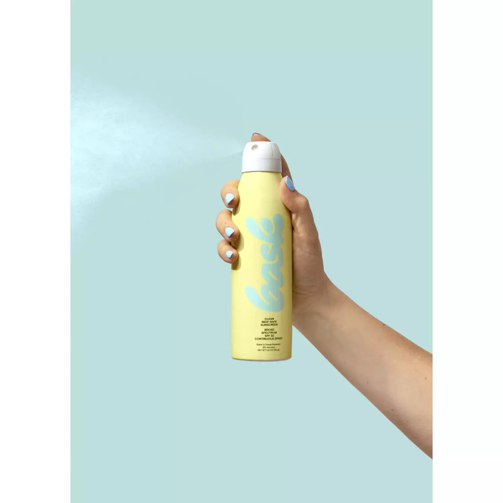 A hand holding a yellow aerosol can against a pastel blue background.